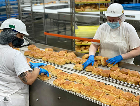 Employees at Baker Boy managing buns on a conveyor belt in a food production facility